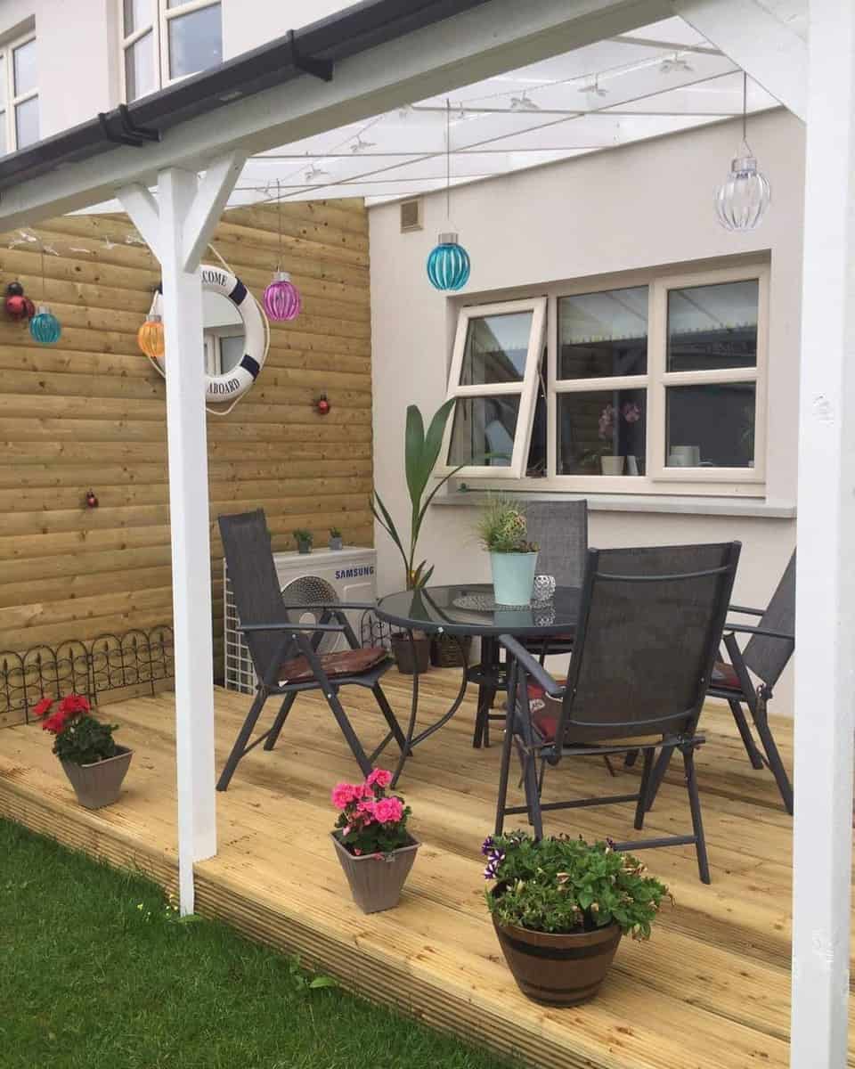 covered wooden terrace, black furniture, potted plants, colorful hanging lamps