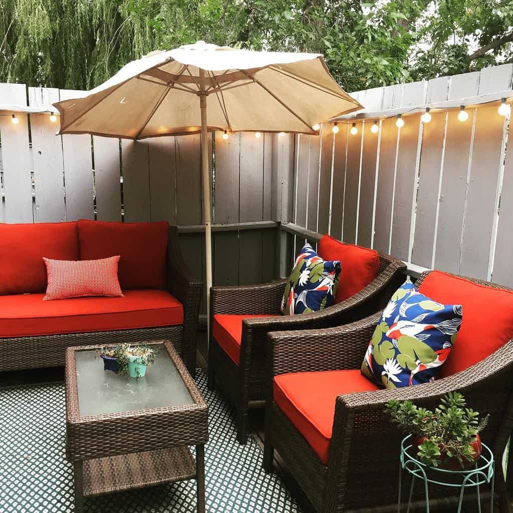 Small wicker chairs in backyard with red cushions and hanging umbrella lamps
